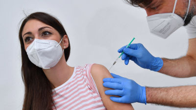 En kvinna i munskydd får coronavaccin av en sjukskötare.