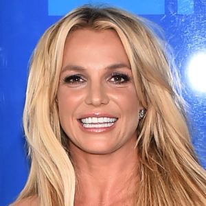 Britney Spears poserar och ler på röda mattan. Hon är klädd i en svart klänning.