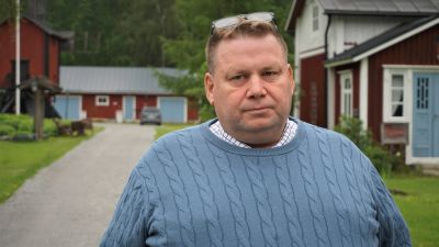 Man i blå tröja står i en trädgård.