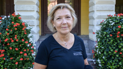 Kvinna står framför ingång med blombuskar bredvid.