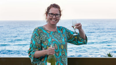 Glad kvinna skålar med vin på en strand.