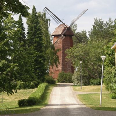 Näkymä Lepaan oppilaitosten pihamaalta kohti Mamselli-tuulimyllyä. Kellarin päällä oleva tiilirakennus pilkottaa tuulimyllyn vasemmalla puolella.
