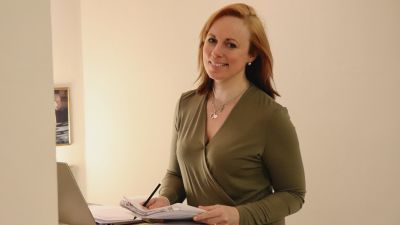 Anna Bertills tittar in i kameran och håller några papper och en penna i händerna.