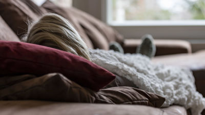 En person ligger på en soffa under en filt.