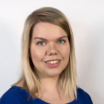Sinisiin pukeutunut toimittaja Anna Nevalainen hymyilee kameralle.
