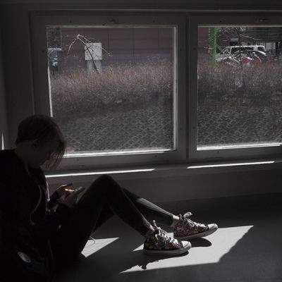 Nuori katsoo kännykkäänsä ikkunan edustalla.