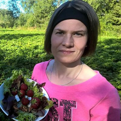 Nainen seisoo mansikkapellolla salaattikulho kädessä.
