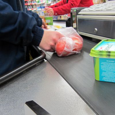 Margariinipaketti ja tomaattipussi kaupan kassan liukuhihnalla.