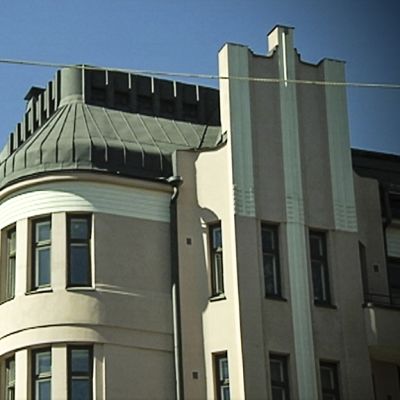 Kivitalo Helsingin keskustassa ja sen pyöreä kulmaus sinistä taivasta vasten.