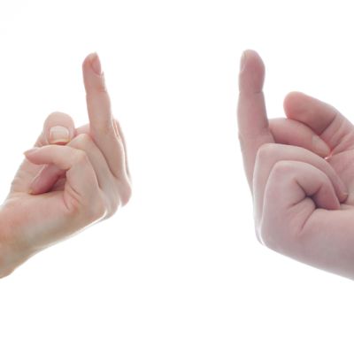 Naisen ja miehen kädet näyttävät toisilleen keskisormea valkoista taustaa vasten.