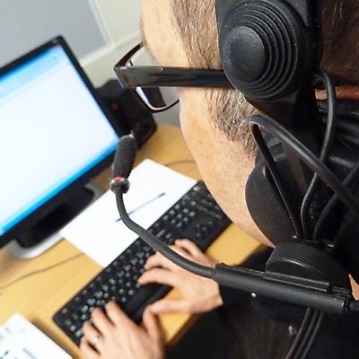 Mies istuu tietokoneen äärellä headset-luurit päässään