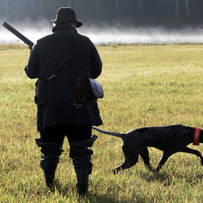Mies metsästää koiran kanssa pellolla.