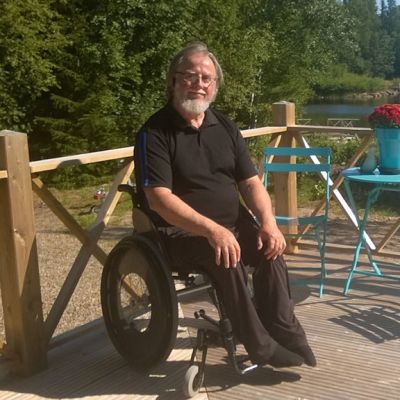 Jorma Aspegren istuu mökkisaunan kuistilla, taustalla merimaisemaa.