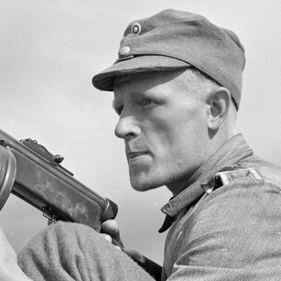 Mies suomalaisessa sotilaspuvussa konepistoolin kanssa.
