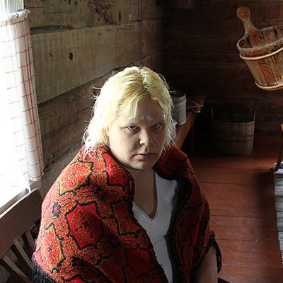 Kuvassa nainen istuu tuvan penkillä