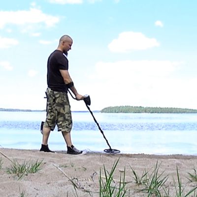 Jarkko Lehtinen haraa metallinpaljastimella rantaa.