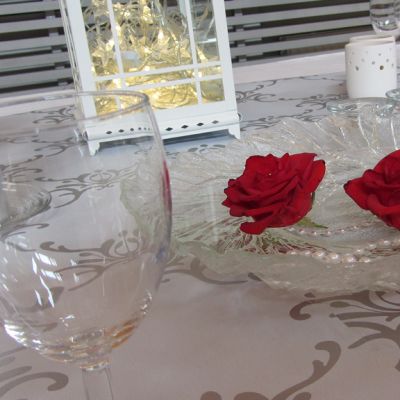Kuvassa vaaleasävyinen kattaus juhlapöydällä, lasien ja lyhtyjen kanssa ruusumalja