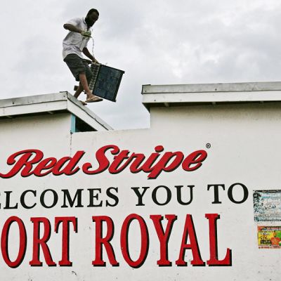 Mies kulkee talon katolla, seinässä teksti 'Red Stripe welcomes you to Port Royal'.