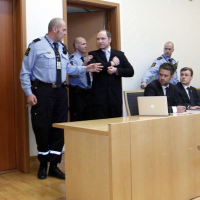 Anders Behring Breivik astuu oikeussaliin poliisisaattueessa.