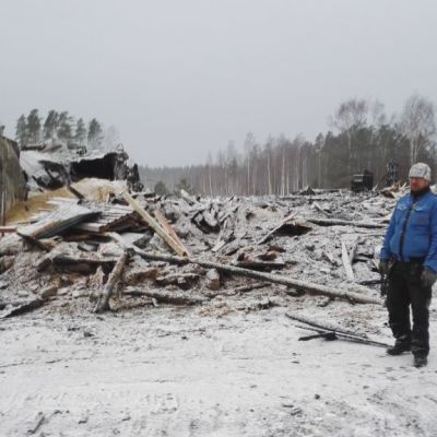 Mies seisoo palaneen sikalarakennuksen raunioiden edessä.