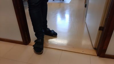 En person med mörka sandaler och strumpor står på en låg tröskel in till ett rum med beige golv.