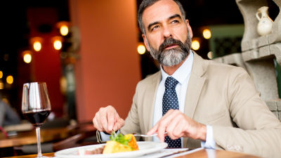 Medelålders man i kavaj och slips sitter på restaurang och äter