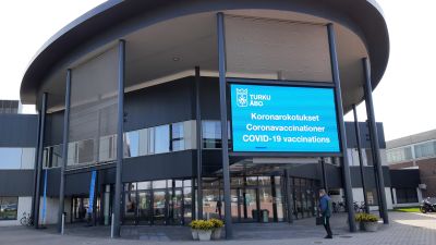 En blå lysande skylt berättar att du ska gå in här för coronavaccinering i Åbo mässcentrum.