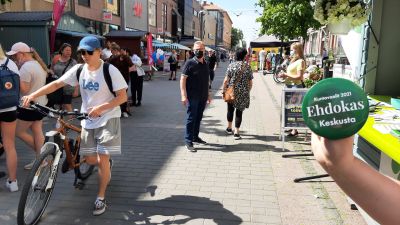 En hand håller på gågatan i Åbo upp en grön reklampins för Centern i samband med kommunalvalet 2021.