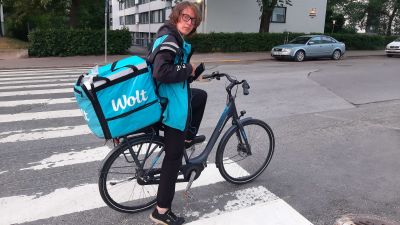 en man med glasögon cyklar med en matleverans i en klarblå låda, där det står Wolt.