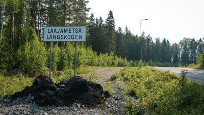 En asfalterad väg i en skog och en skylt där det står Laajametsä/Långskogen.