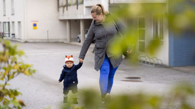 En kvinna går på en parkering och håller sin ettåriga son i handen.