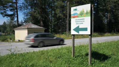 Silverfärgad bil kör förbi en skylt vid vägen.