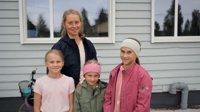 Kvinna med tre barn står framför en vit byggnad.