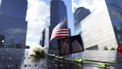 Bild på blomma och USA:s flagga mot minnesmärke vid Ground Zero.