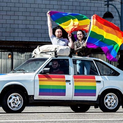 Ohiajavassa autossa ihmiset heilittavat sateenkaarilippuja