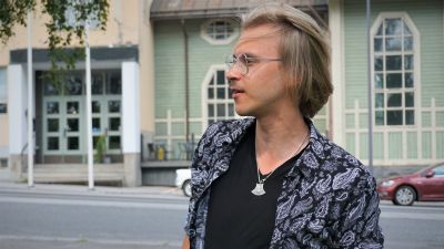 Ung blond man med glasögon står vid en gata.
