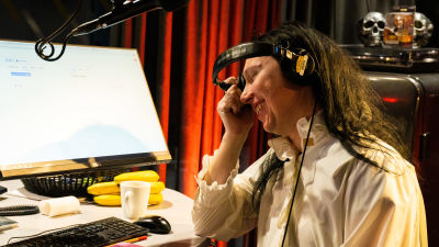 En svarthårig man skrattar i en radiostudio med ett par hörlurar på huvudet.