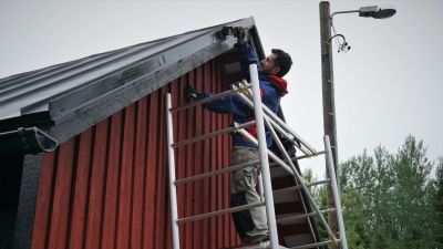 En man står på en byggställning och målar taket på ett hus.