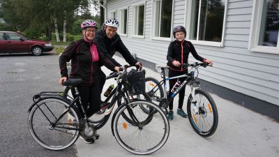 En familj på cykel står framför en vit byggnad.