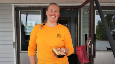 Kvinna i gul tröja står med en hotdog i handen.