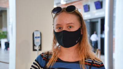 Silja Järvinen med solglasögon på huvudet och svart munnskydd inomhus.