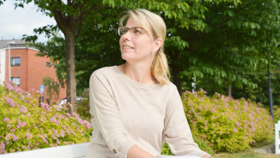Johanna Tamminen sitter på en bänk i en park i beige tröija.
