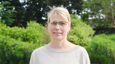 Johanna Tamminen utomhus i en grön miljö i beige tröija.
