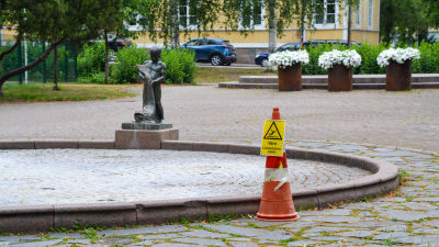Vattenfontänen i stadsparken i Borgå utan vatten i sig. Bredvid fontänens bassäng står en skylt som varnar för halt botten.