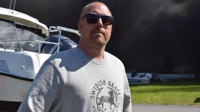 En man i solglasögon och en grå collegetröja står framför en båt.