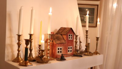 Ett miniatyrhus samt flera ljus står på spiselkransen.