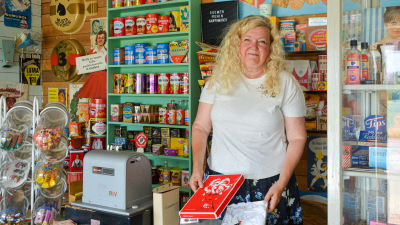 Minna Järvinen står bakom kassan i en butiksmiljö från 50- och 60-talet.
