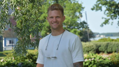 En man med kort blont hår och vit t-skjorta står ute vid en park. Det är Stallörsparken i Ekenäs och det är sommar och sol. Han tittar rakt in i kameran och ler
