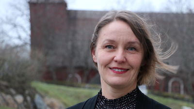 En kvinna med axellångt mörkt hår. I bakgrunden syns en gammal röd träkyrka.
