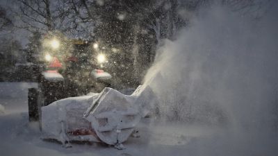 Traktor med snöplog som sprutar snö.